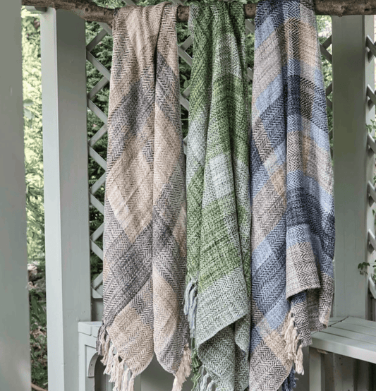Three patterned throw blankets hanging on a wooden branch outdoors.