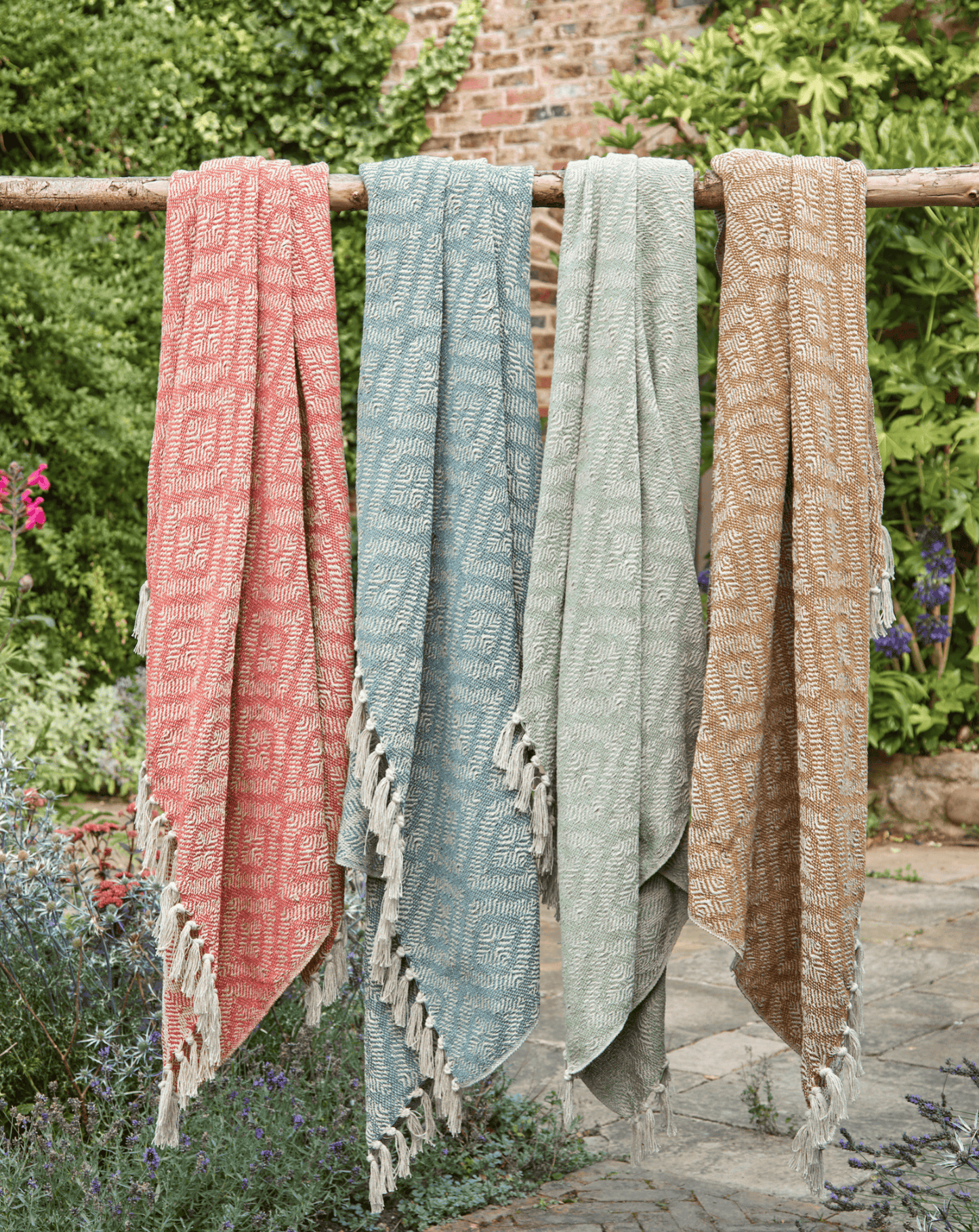Three patterned towels hanging on a wooden rack outdoors with greenery in the background.