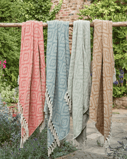 Three patterned towels hanging on a wooden rack outdoors with greenery in the background.