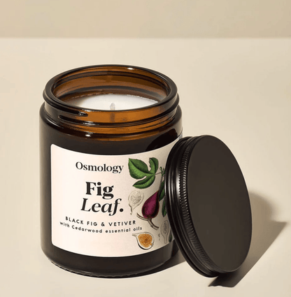 Osmology Fig Leaf candle in a glass jar with a black lid on a beige background