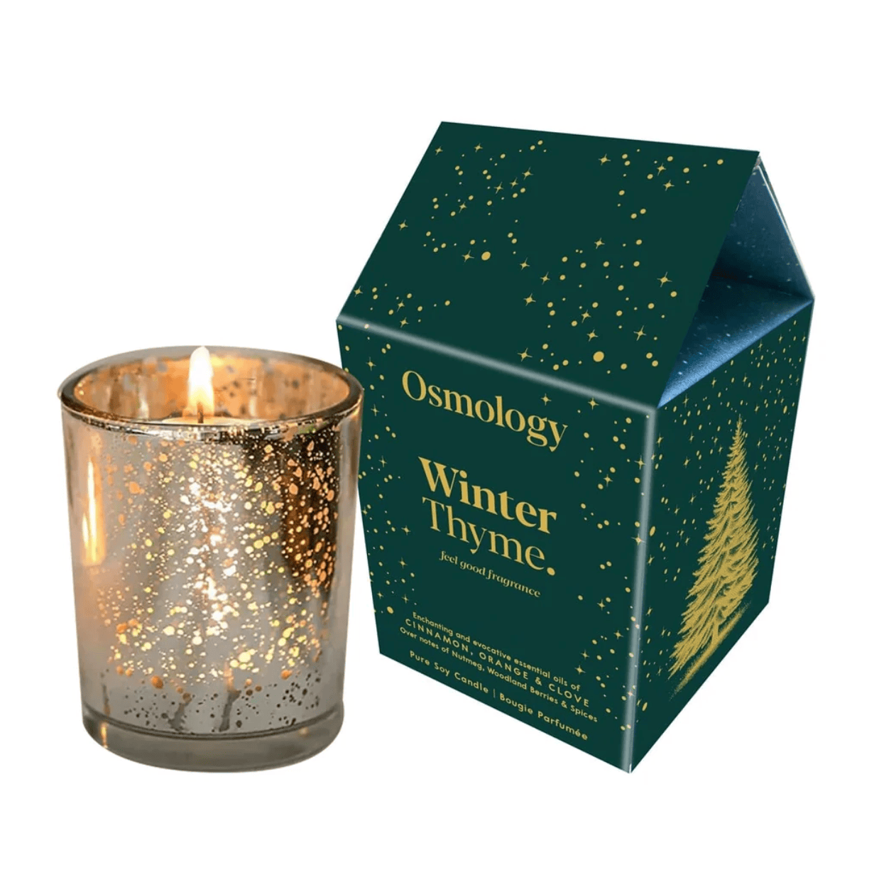 A lit Osmology Winter Thyme candle in a clear glass vessel with gold glitter, shown next to its dark green house-shaped packaging box with gold star and tree details.