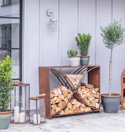 Wooden firewood holder with stacked logs outdoors, surrounded by potted plants and lanterns.