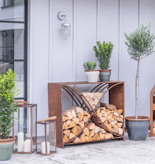 Wooden firewood holder with stacked logs outdoors, surrounded by potted plants and lanterns.