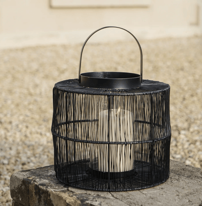 Black woven lantern with a handle on a stone surface against a beige wall.