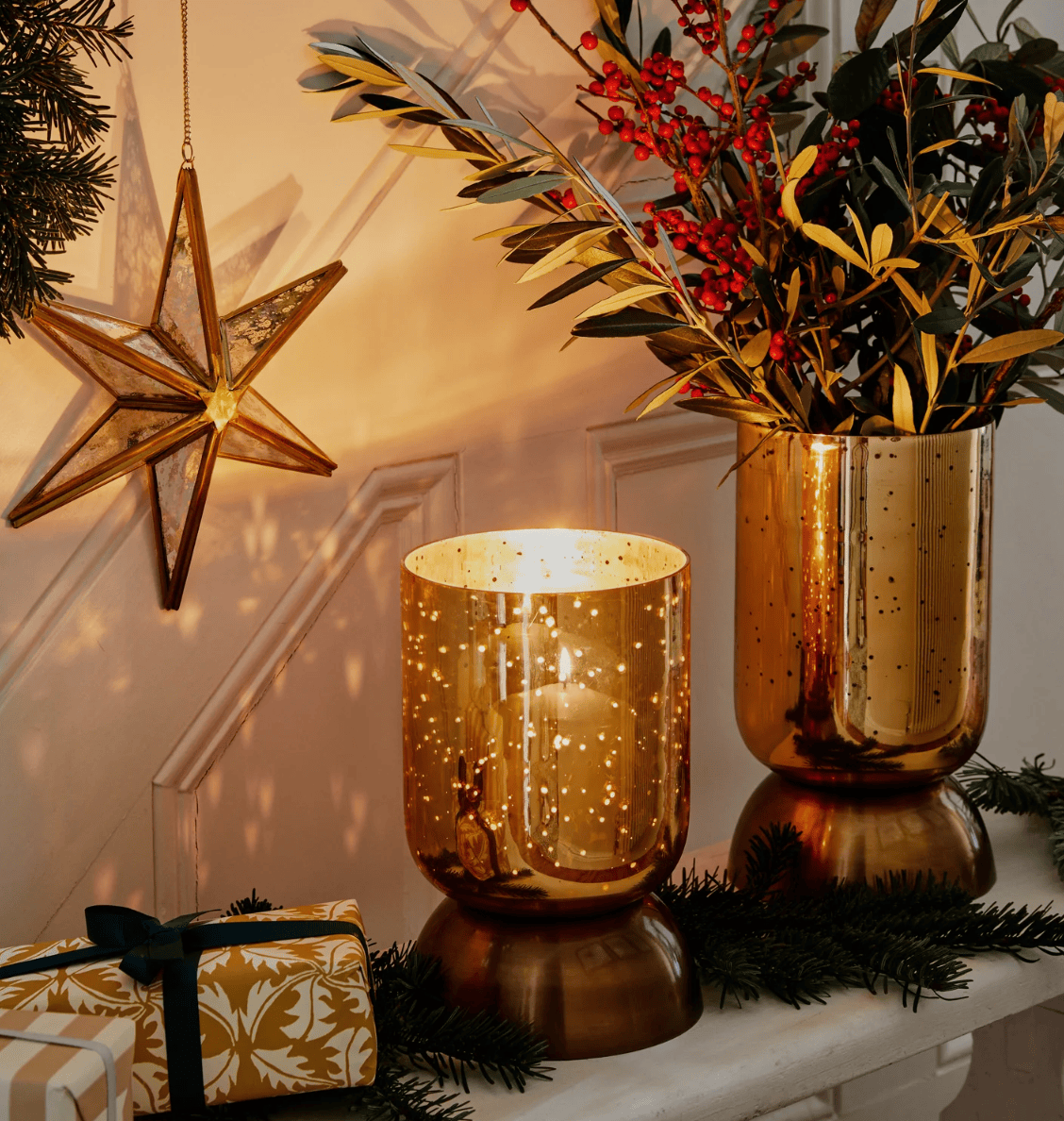 Decorative setup with gold candle holders, a vase with greenery, and a star ornament on a white surface.