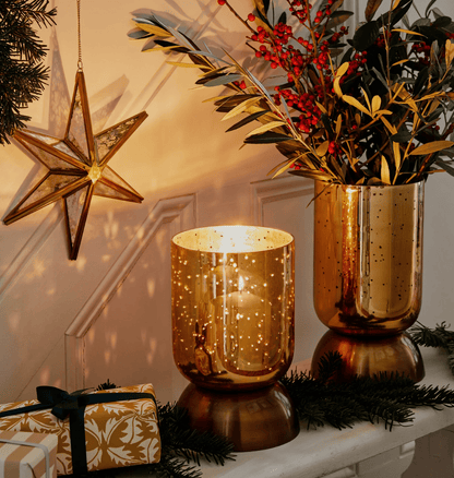 Decorative setup with gold candle holders, a vase with greenery, and a star ornament on a white surface.
