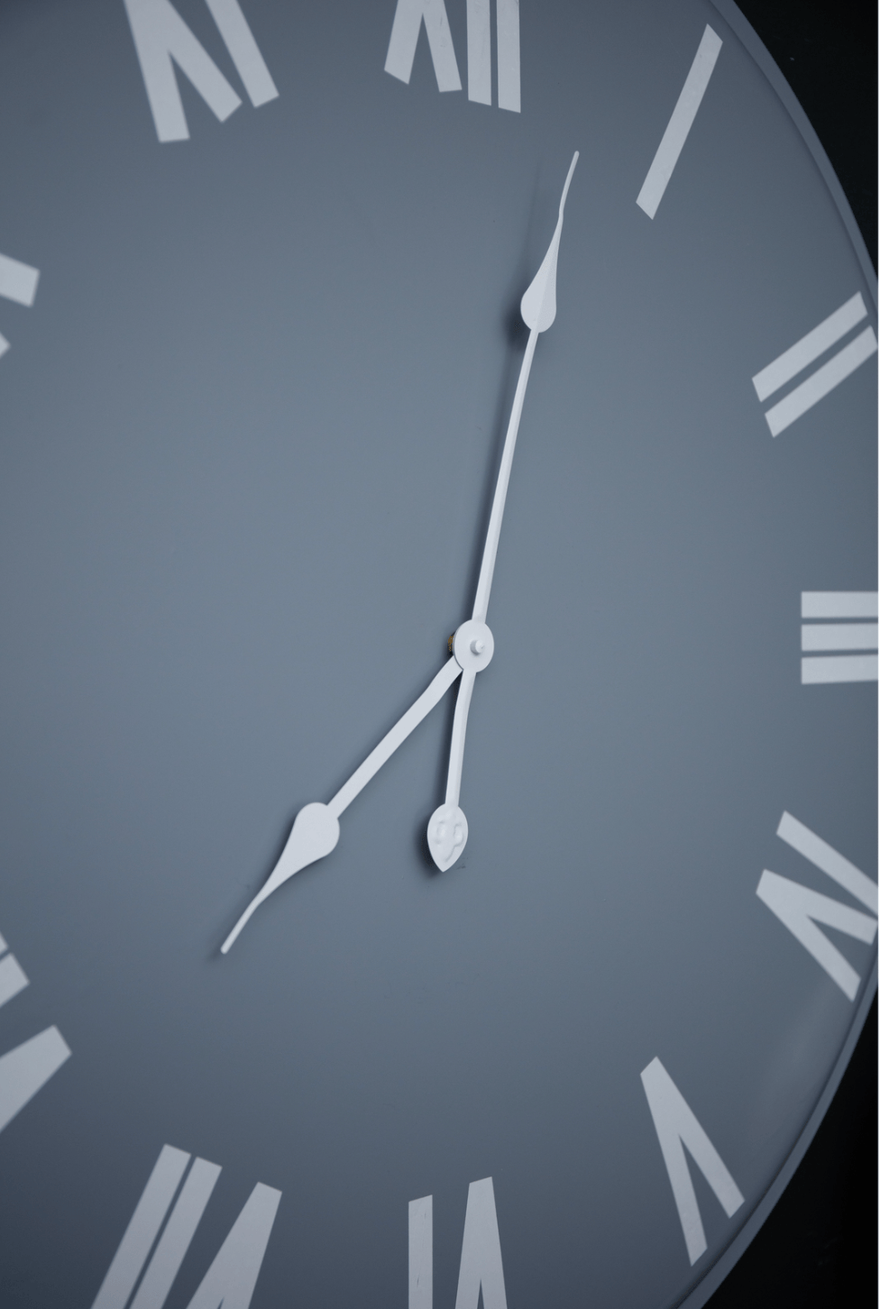 Close-up of a clock face with Roman numerals on a grey background