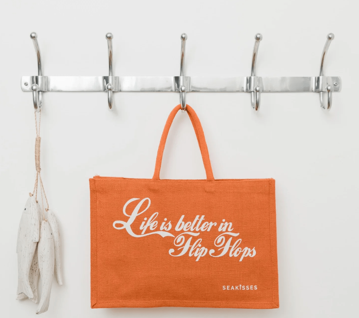Orange tote bag with 'Life is better in Flip Flops' text hanging on a wall hook.
