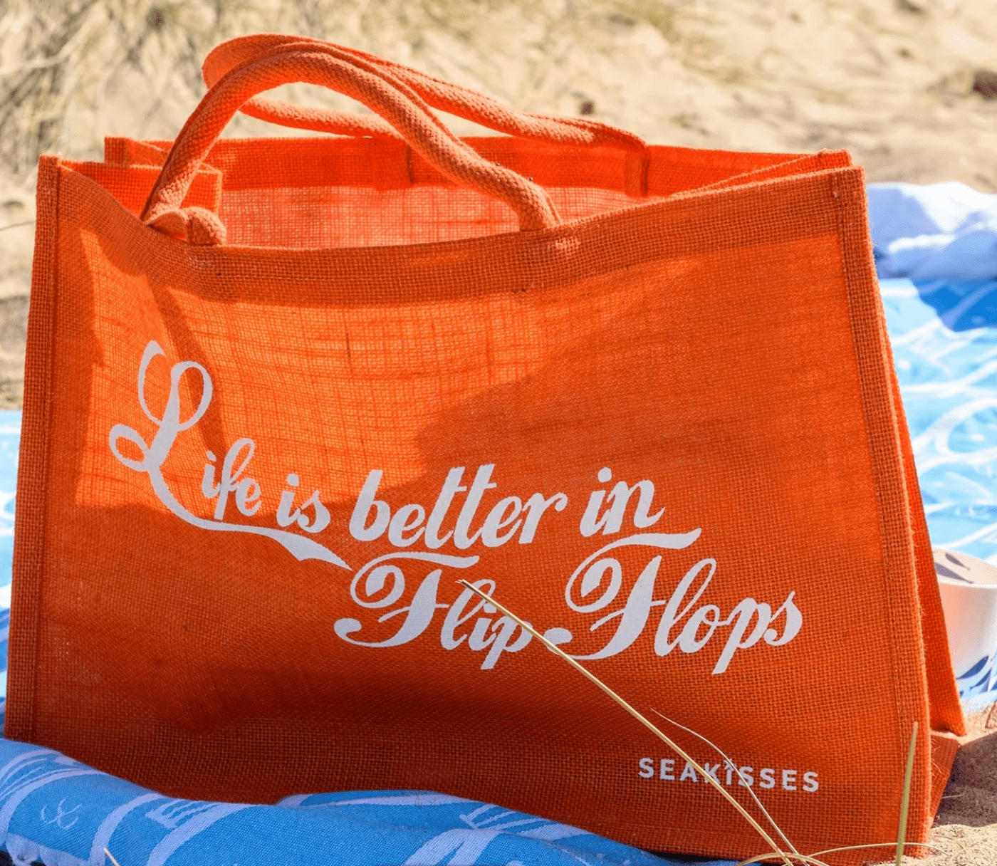 Orange tote bag with 'Life is better in Flip Flops' text on a beach setting