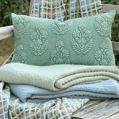 Green textured pillow and blanket on a wooden bench with a patterned fabric background.