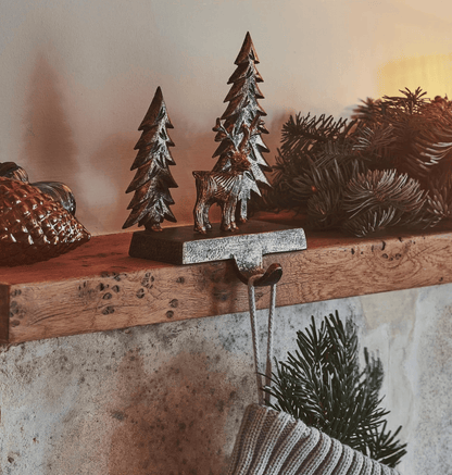 Decorative Christmas trees and a deer figurine on a wooden mantel with a warm glow.