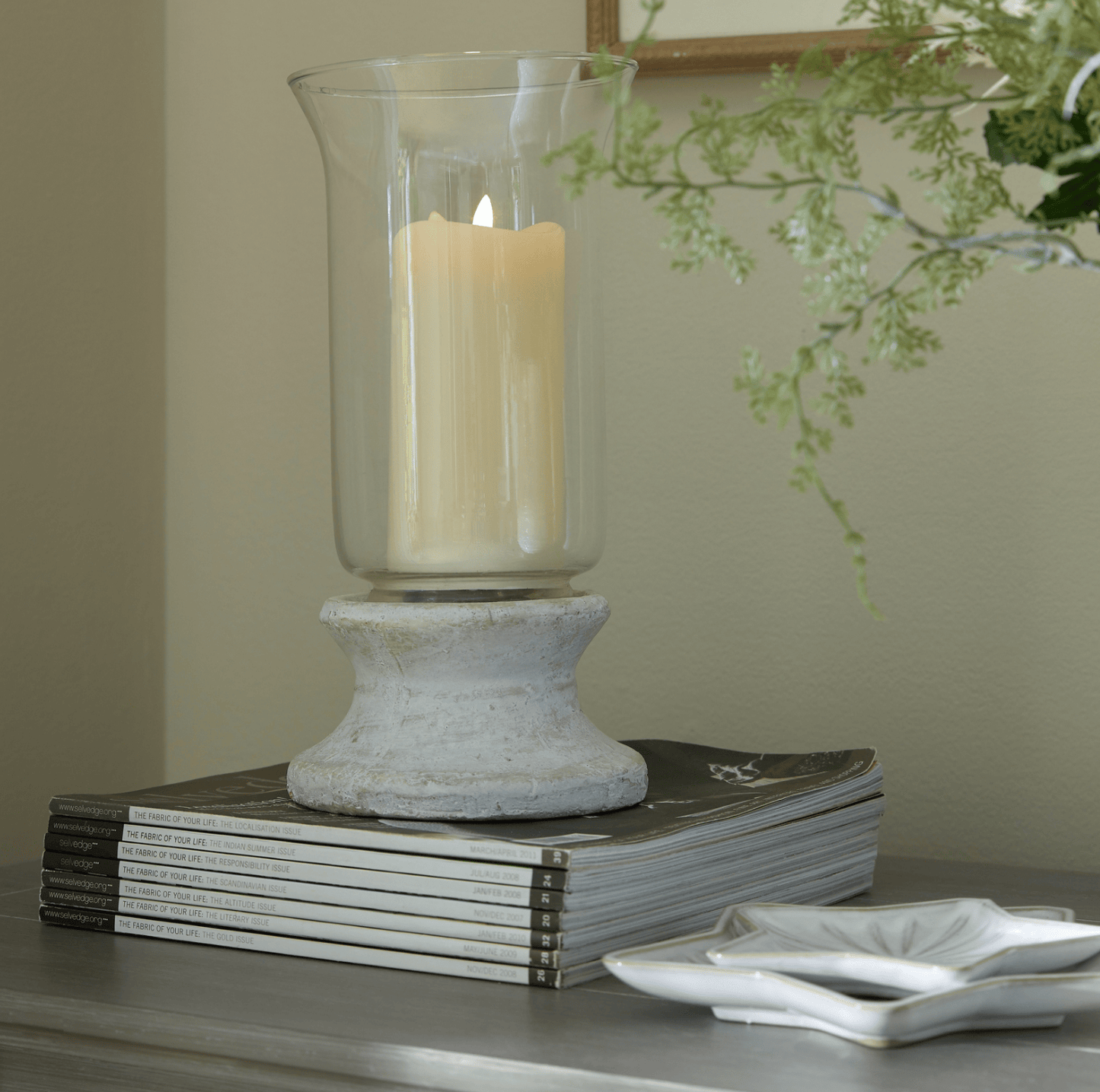 Candle in a glass holder on books with a decorative branch in the background