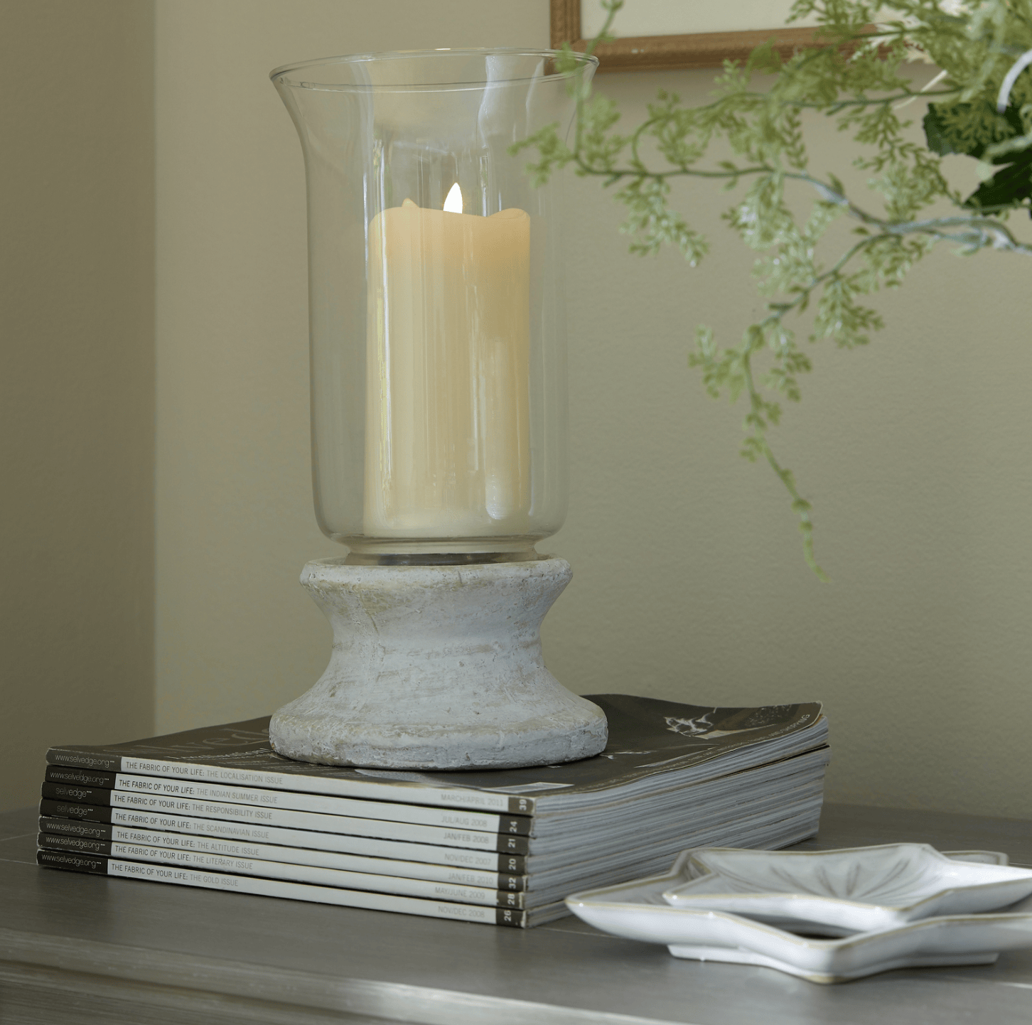 Candle in a glass holder on books with a decorative branch in the background