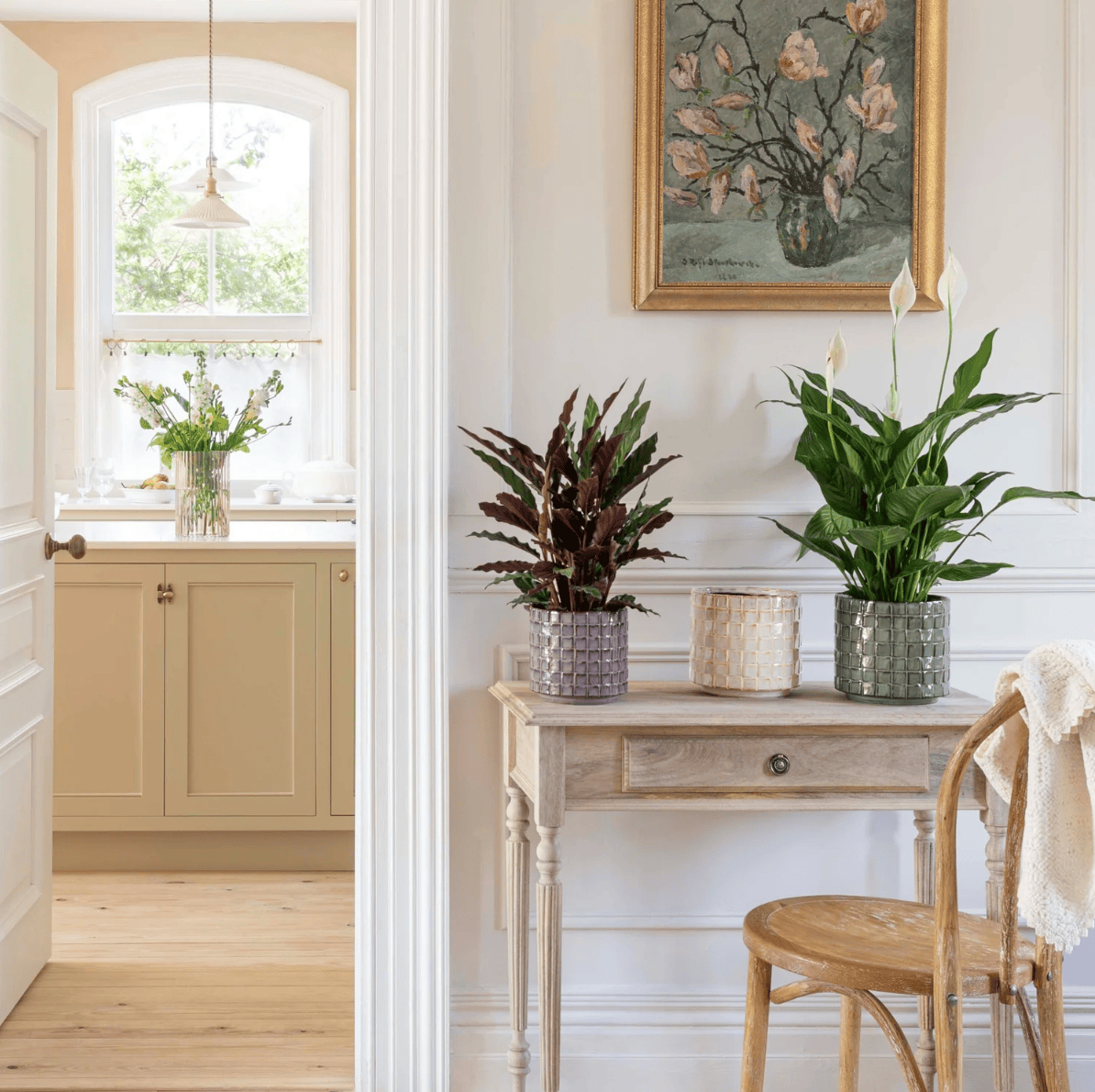 Nest living room with plants, a desk, and a painting on the wall.