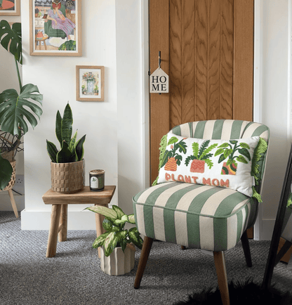 Green and white striped armchair with a 'Plant Mom' pillow in a room with plants and a wooden door.