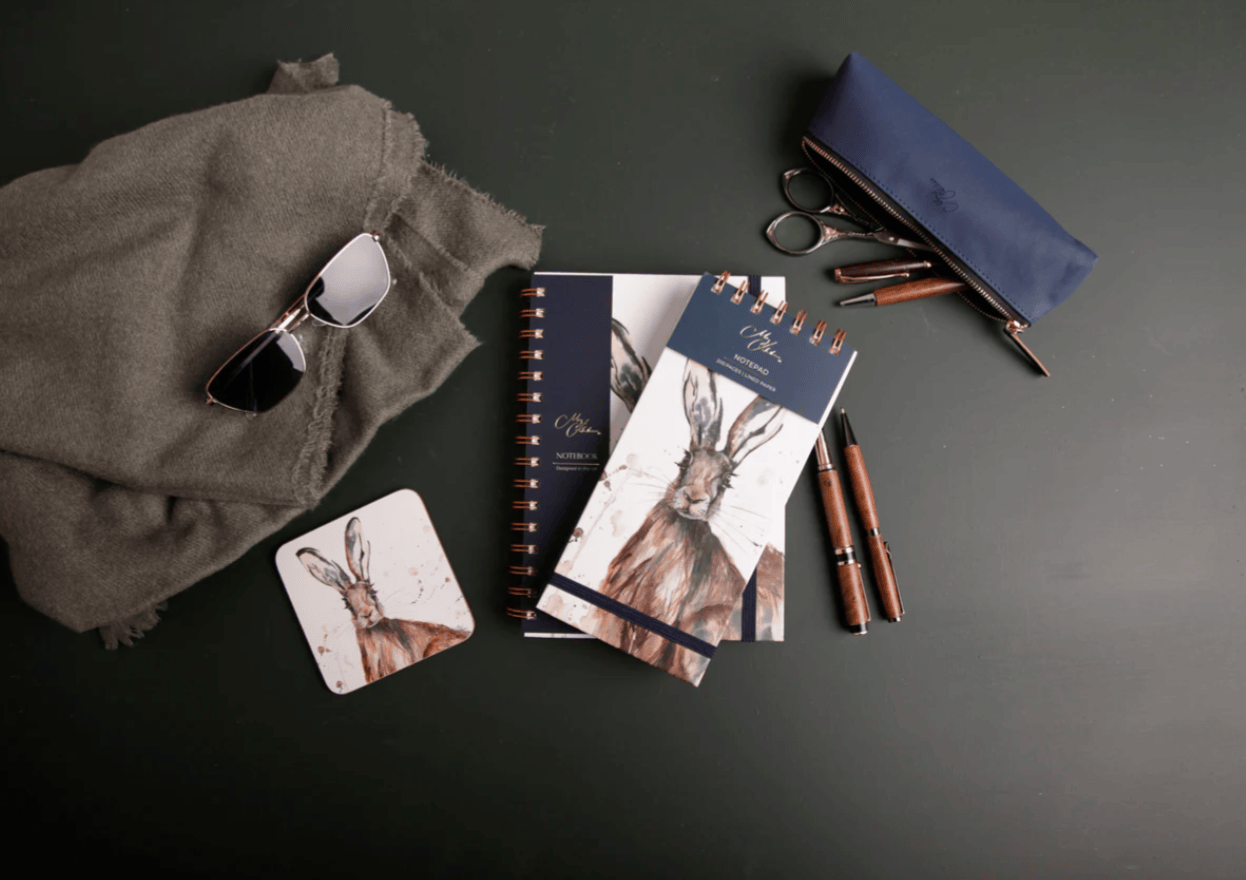 Collection of stationery items including notebooks, pens, and sunglasses on a dark surface