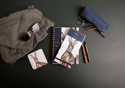 Collection of stationery items including notebooks, pens, and sunglasses on a dark surface