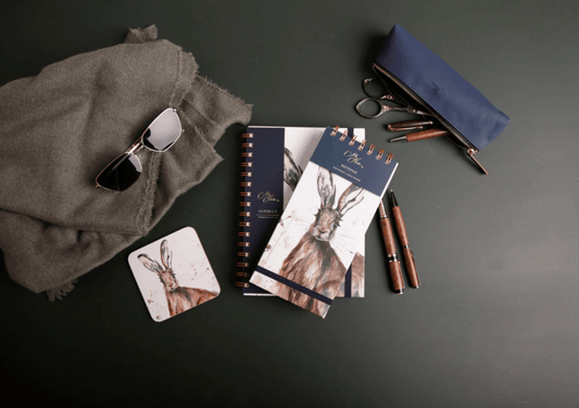 Collection of stationery items including notebooks, pens, and sunglasses on a dark surface