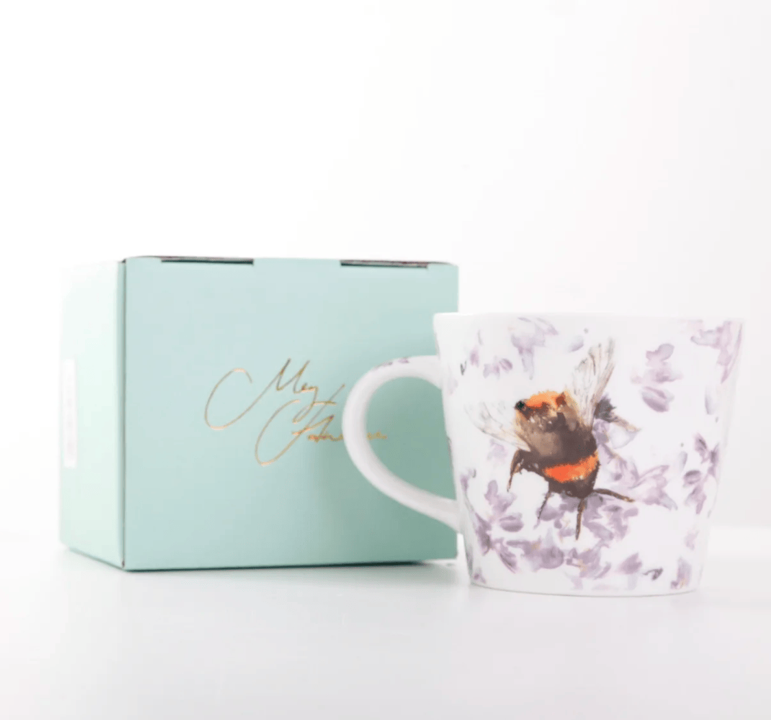 A white ceramic mug with a purple floral print and a bumblebee illustration, shown next to its light blue gift box with gold cursive lettering on a white background.