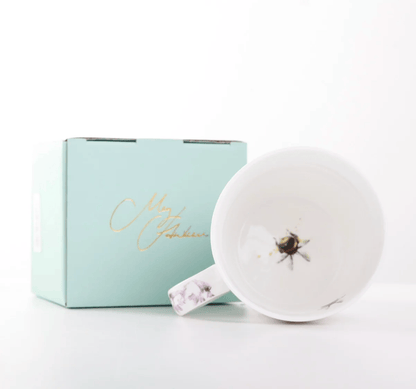 A white ceramic mug with a floral-patterned handle and a printed bee design inside the cup, shown next to its light blue gift box with gold script lettering on a clean white background.