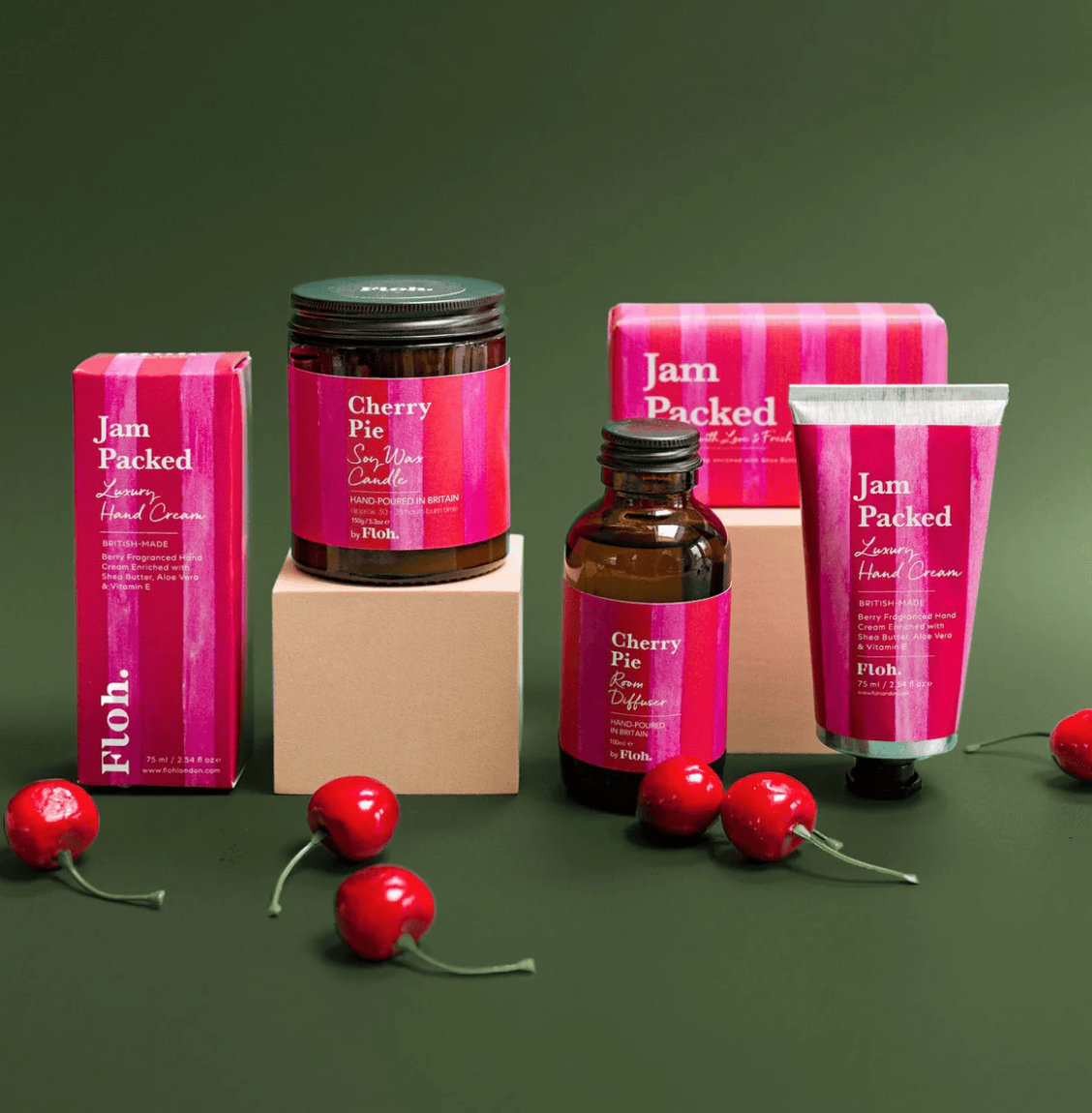 Collection of 'Jam Packed' skincare products with cherry-themed packaging on a green background.