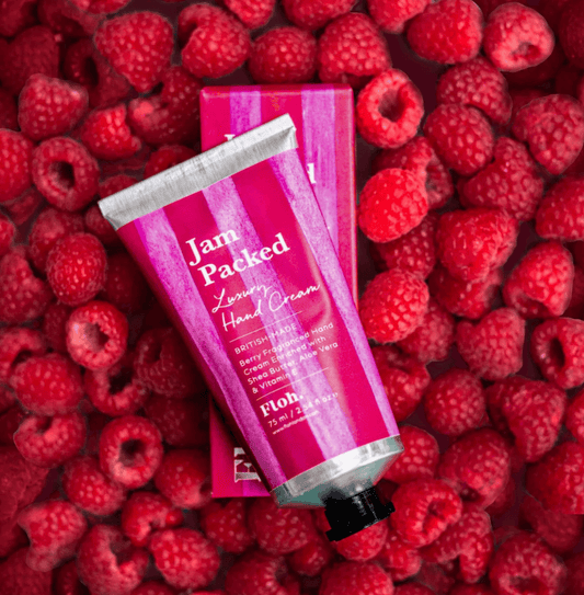 Hand cream tube labeled 'Jam Packed' on a bed of raspberries