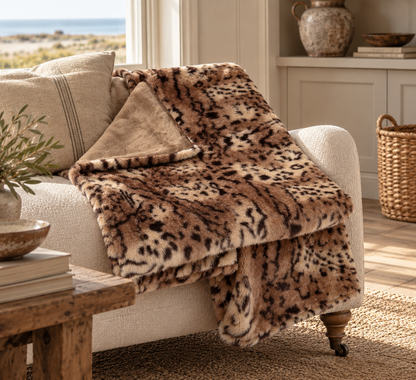 A plush throw blanket with a brown, beige, and black leopard print pattern draped over a cream-colored armchair in a sunlit living room.