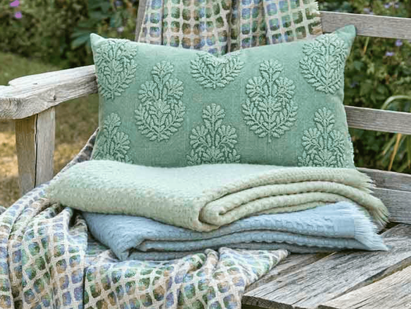 Green textured pillow and blanket on a wooden bench outdoors