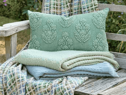 Green textured pillow and blanket on a wooden bench outdoors
