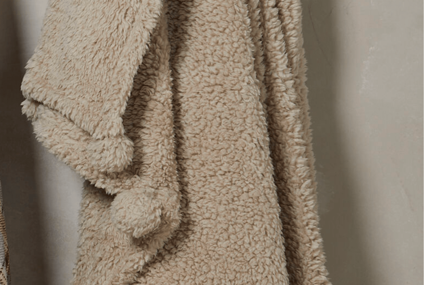 Beige textured blanket with pom-poms on a neutral background