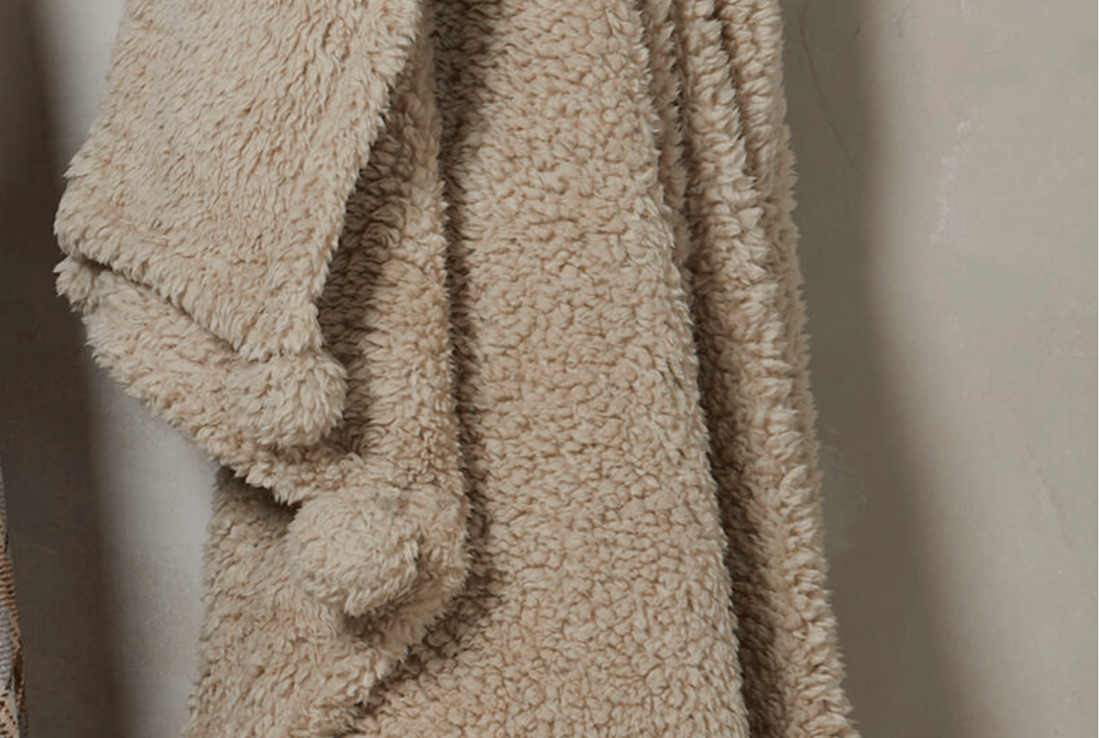Beige textured blanket with pom-poms on a neutral background