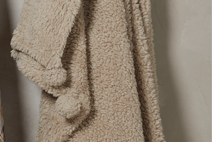 Beige textured blanket with pom-poms on a neutral background