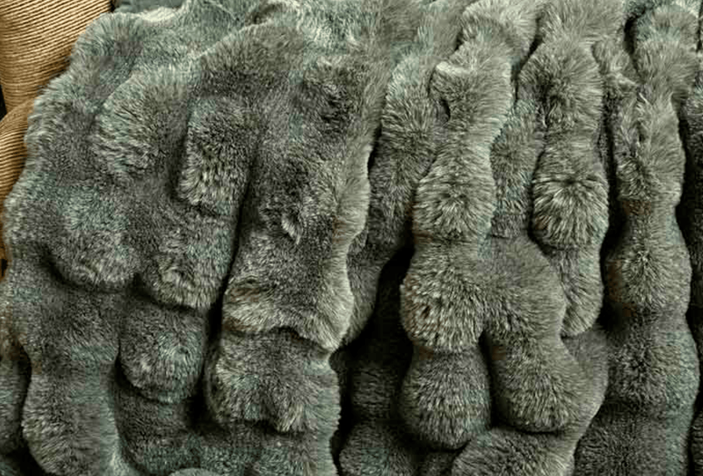 A close-up of a plush, textured faux fur or rabbit fur blanket in a muted gray-green color, showing the soft, wavy pile of the material.