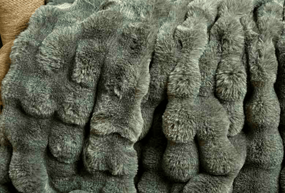 A close-up of a plush, textured faux fur or rabbit fur blanket in a muted gray-green color, showing the soft, wavy pile of the material.