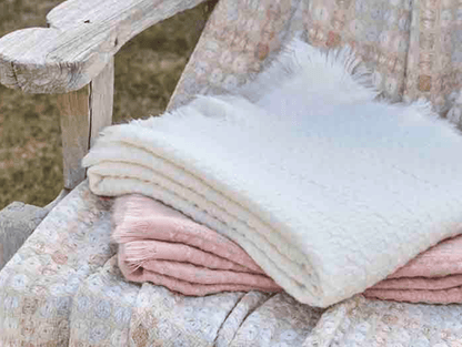 Folded blankets in pastel colors on a wooden bench outdoors