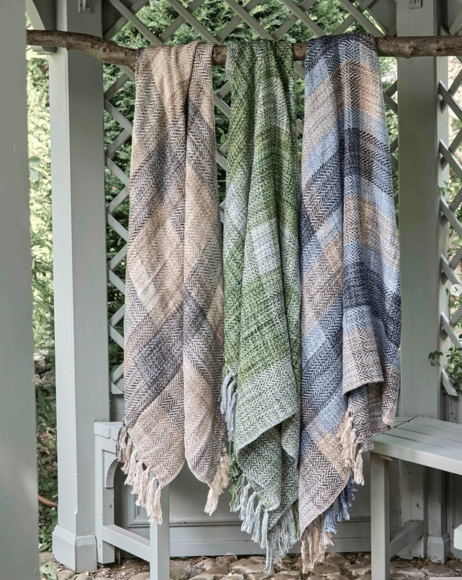 Three patterned blankets hanging on a wooden rack outdoors.