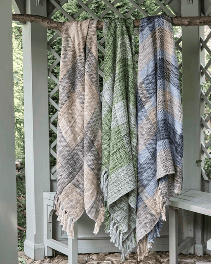 Three patterned blankets hanging on a wooden rack outdoors.