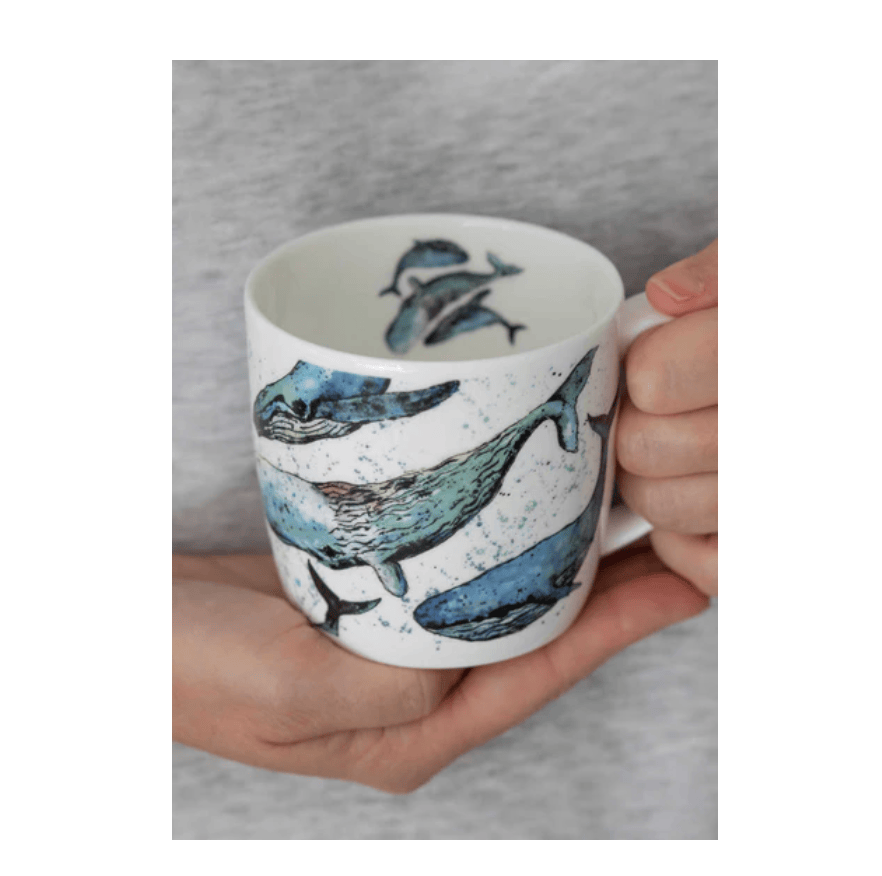 Hand holding a mug with whale design against a gray background